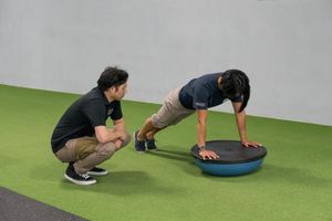 Vince from Catalyst physio working with a client. The client is holding a push-up position on a bosu ball.